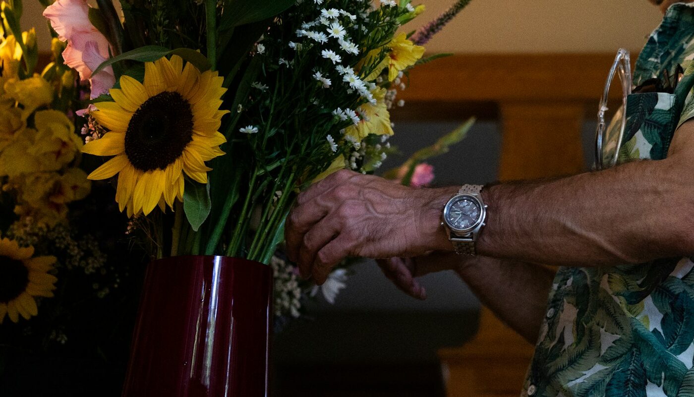 Verzorgende neemt in een huiskamer een bos bloemen in ontvangst van een oudere vrouw, gezicht niet herkenbaar