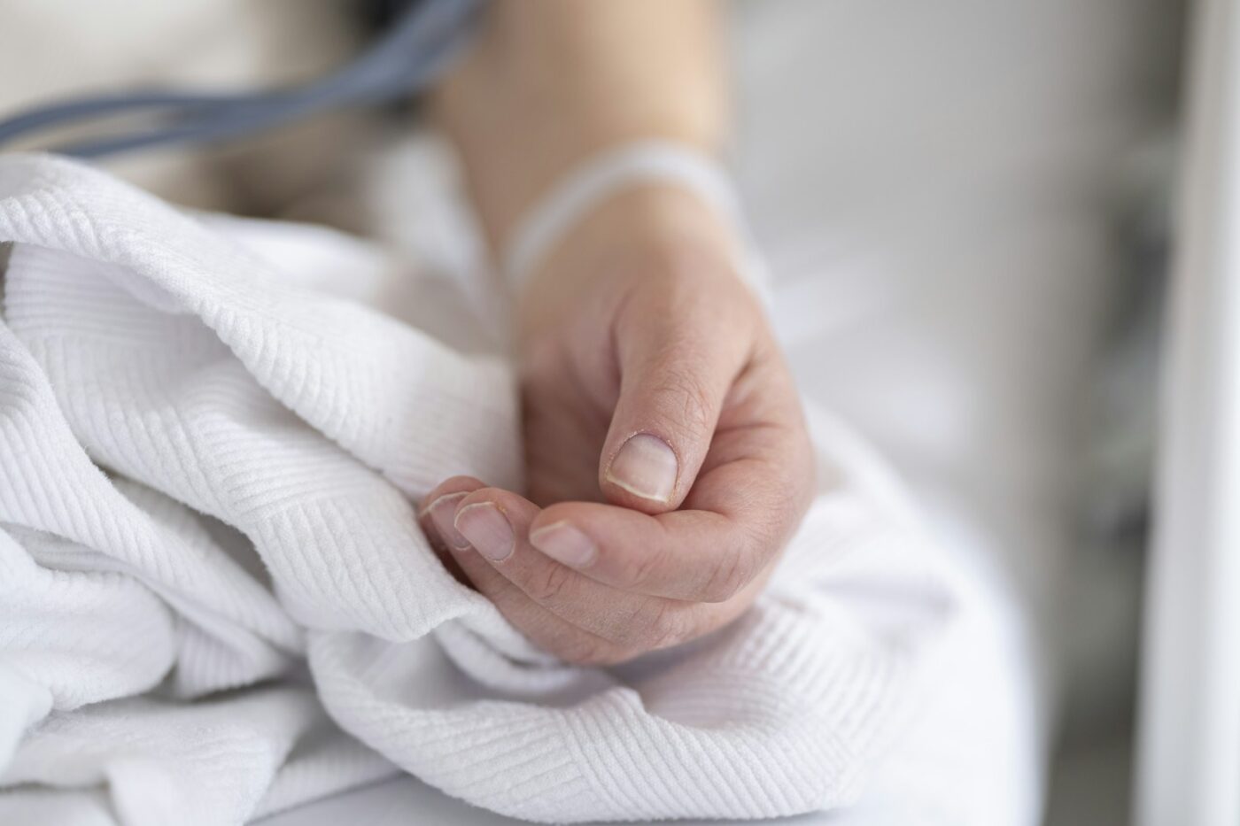 Hand van een zorgverlener op de hand van een oudere patiënt in bed