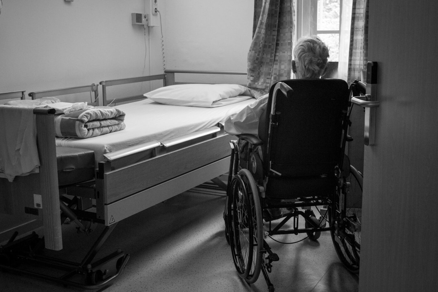 Verpleegkundige zit naast het bed van een oudere patiënt en praat rustig met hem